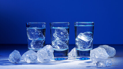 Glass of vodka with ice on blue background, selective focus