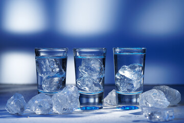 Glass of vodka with ice on blue background, selective focus