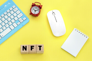 Wooden cubes with word NFT. Notepad, Alarm clock, keyboard, mouse on the background.