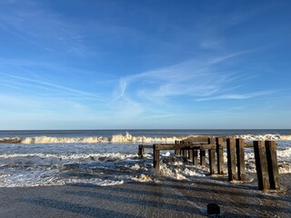 Landscape of ocean from sandy beach he beautiful calm sea gentle waves and blue skies looking to horizon with wood defence structure from shore on bright cold Winter day Norfolk uk 