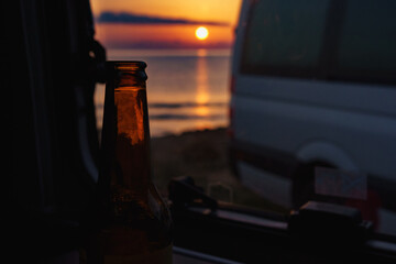 Enjoying a beer from inside a motorhome, while the sun sets by the sea.