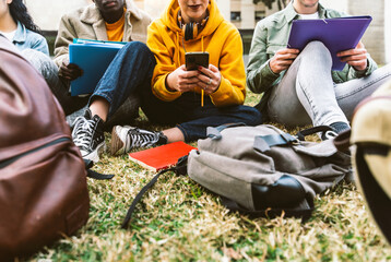 Fototapeta International students sitting together on green campus lawn - Group of high school teens studying outside college - Multiethnic millenial friends doing homework in university park - Academic concept obraz