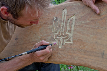Woodwork. man cuts out the coat of arms of Ukraine on the bench.