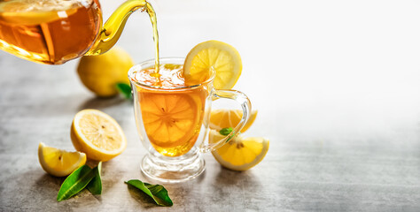 iced lemon fruit tea pouring in a glass cup from tea pot isolated over plain grey background, no people. food summer refreshment concept