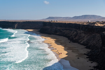 Naklejka premium Vista panoramica de una playa salvaje con un grupo de personas aprendiendo a hacer surf cerca de El Cotillo, Fuerteventura, Islas Canarias, España