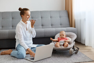 Horizontal shot of satisfied Caucasian woman with bun hairstyle wearing white shirt and jeans,...