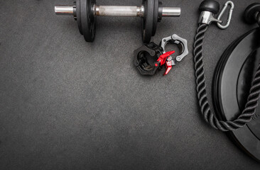 Obraz na płótnie Canvas Barbell, dumbbells, triceps rope and clamps on the floor at the gym. Top down view flat lay with bodybuilding equipment on a black background and empty space for text. Fitness, weight training concept