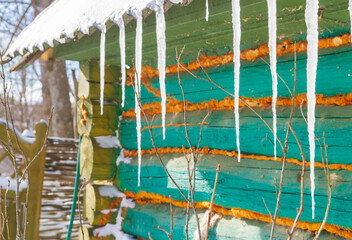 Icicles hang from the roof of an old wooden house - 488169397