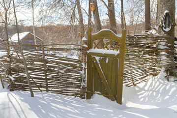 Wooden fence made of sticks with a wooden door in the yard in winter - 488169505