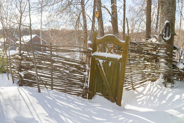 Wooden fence made of sticks with a wooden door in the yard in winter - 488169521