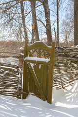Wooden fence made of sticks with a wooden door in the yard in winter - 488169561