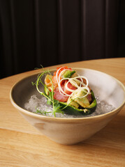Avocado appetizer stuffed with canned salmon, red caviar, avocado slices, greens. Stuffed avocado served on ice. The concept of dietary nutrition. Gourmet restaurant appetizer. Copy space. Close up.