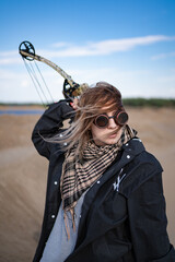A girl archer in steampunk goggles and with a block bow in a post-apocalyptic image in the desert....
