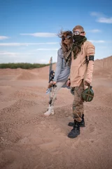 Tuinposter Couple in futuristic clothes in the desert. The woman has a bow, arrows and steampunk goggles, the man has a flask and a telescope. Post-apocalyptic cosplay of an archer and a nomad, artistic staged © evgenzz