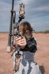 A girl archer in steampunk goggles and with a block bow in a post-apocalyptic image in the desert....