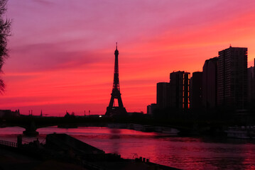 Urban landscape. View on the Eiffel tower with group of modern buildings in front of the water of Seine river. Dramatic sky with colorful clouds. Silhouette of a cityscape at sunrise.	