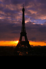 Naklejka premium Silhouette of the Eiffel tower with dramatic sky in the background. Orange clouds at sunset or sunrise. Vertical plan.
