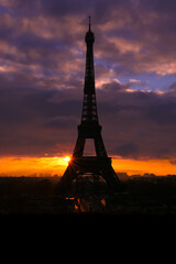 Naklejka premium Silhouette of the Eiffel tower with dramatic sky in the background. Orange clouds at sunset or sunrise. Vertical plan.