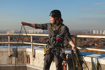 Industrial climber unwinds a rope and smiles on the roof of a building