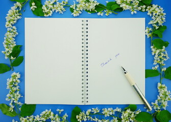 Notebook on a blue background with white bird cherry flowers. Top view, copy space, flat lay.	