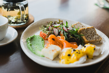 Light and hearty breakfast, brunch with scrambled eggs, toast on grain bread and smoked salmon and guacamole. Served with a mix of arugula and radish