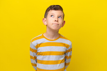 Little caucasian boy isolated on yellow background and looking up