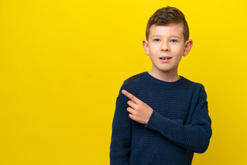 Little caucasian boy isolated on yellow background surprised and pointing side