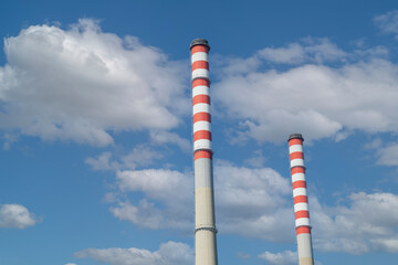 Close up of two factory chimneys with red and white stripes with a cloudy blue sky in the background