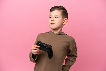 Little caucasian boy playing with a video game controller isolated on pink background suffering from backache for having made an effort