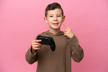 Little caucasian boy playing with a video game controller isolated on pink background giving a thumbs up gesture