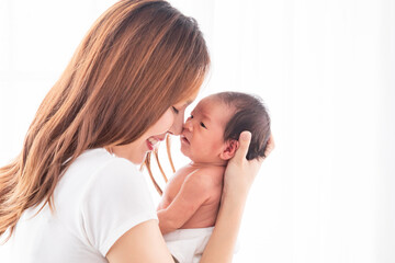 Beautiful Asian mother holding her baby in her arm and put her nose on baby's nose. Touching of love between mom and child concept, infant and mother concept.
