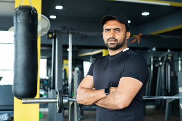 Portrait shot of gym trainer or coach standing at gym with crossed arms by looking camera - concept...