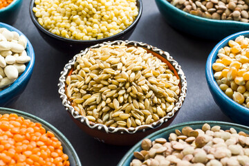 Uncooked dry cereal food group in  ceramic bowls on black surface.Selected wheat bowl