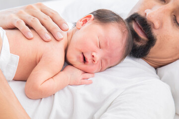 Fototapeta na wymiar Close up of Asian newborn baby sleeping on his father's chest. Dad and son spend time together at home, young dad with cute little infant in his arms. Father and toddler in bed in the morning