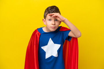 Little caucasian boy isolated on yellow background in superhero costume and showing something