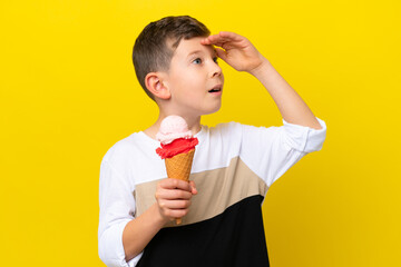 Little caucasian boy with a cornet ice cream isolated on yellow background doing surprise gesture...