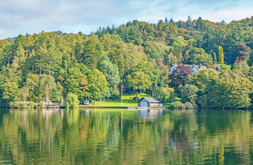 Fototapeta na wymiar The beautiful white house and boathouse stunningly reflected on the rippling lake