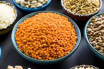 Uncooked dry cereal food group in  ceramic bowls on black surface.Selected red lentil bowl