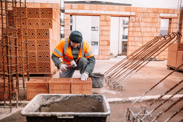 Close up details of mason working with bricks, mortar, cement and rubber hammer on construction site