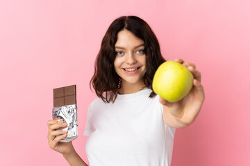 Teenager Ukrainian girl isolated on pink background taking a chocolate tablet in one hand and an...