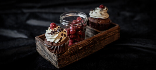 Schwarzwald Food Fotografie dunkel - Schwarzwälder Kirschtorten Cupcakes / Muffins und Glas mit Kirschen in alter rustikaler Holzkiste auf Tisch mit schwarzer Tischdecke