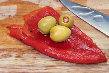 Green stuffed olives and red bell pepper in cutting board.