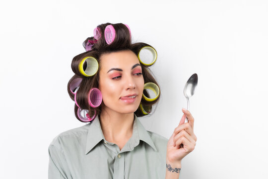 Beautiful housewife. Young cheerful woman with hair curlers, bright make-up, with a tablespoon in her hands, on a white background. Yummy, lick lips