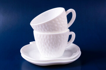 Two beautiful white cups (mugs) in the shape of strawberries and two saucers are stacked on top of each other on a dark blue background. Empty clean dishes.