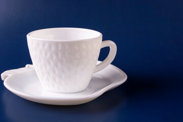 A beautiful white cup (mug) in the shape of a strawberry on a saucer on a dark blue background. Empty clean dishes. Space for text.