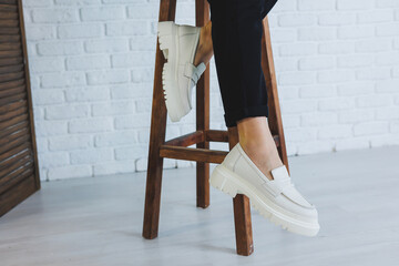 Legs of a young beautiful woman in black trousers and modern stylish white leather loafers. New...