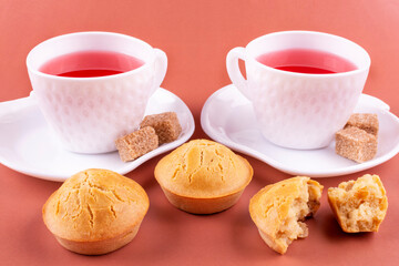 Homemade rice cupcakes with raisins on a white plate, two cups of raspberry tea, brown sugar on a pink background. Rice flour muffins. The concept of proper nutrition. Gluten-free breakfast.