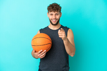 Obraz premium Handsome young man playing basketball isolated on blue background surprised and pointing front
