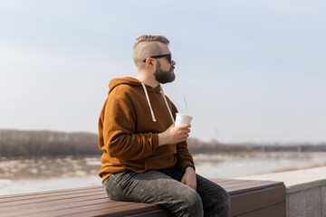 Bearded man drinking a shake in spring promenade. Drinks take away and gen z or millennial youth concept. Copy space for advertising