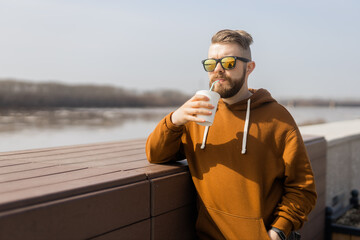 Bearded man drinking a shake in spring promenade. Drinks take away and gen z or millennial youth...